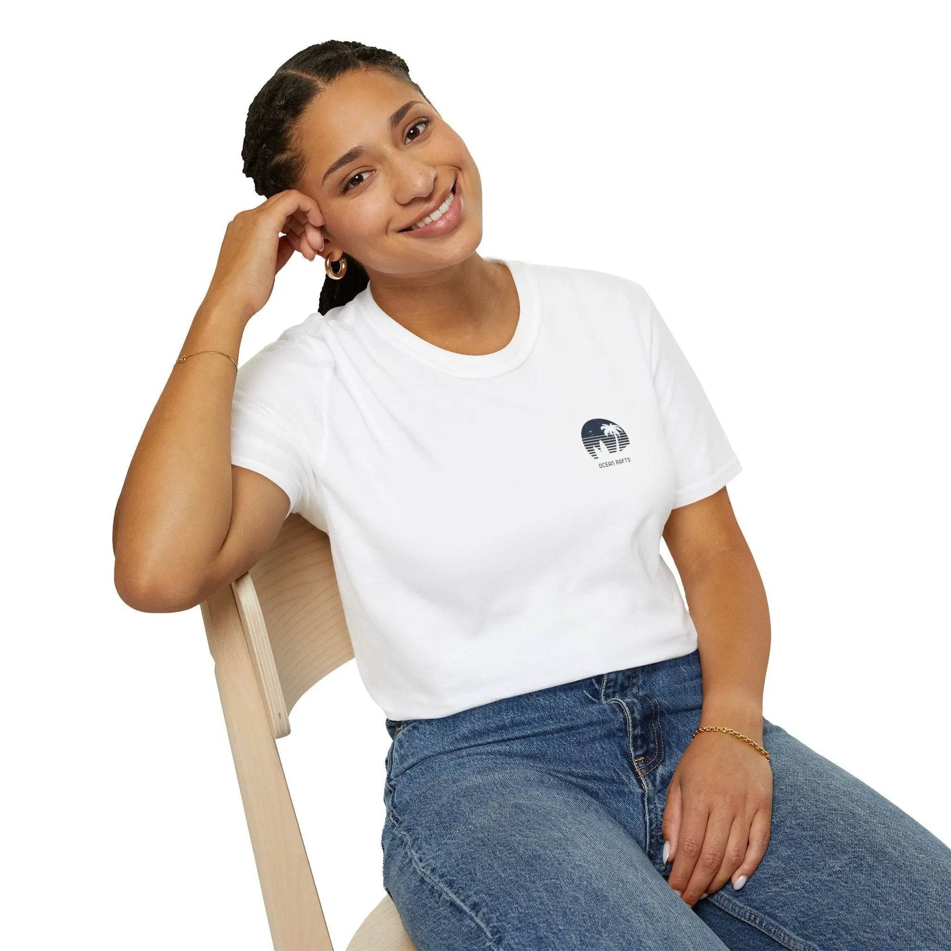 a woman sitting on a chair with a smile on her face wearing shirt with a picture of a surfboard and palm trees in a circular eblem | Ocean Rafts