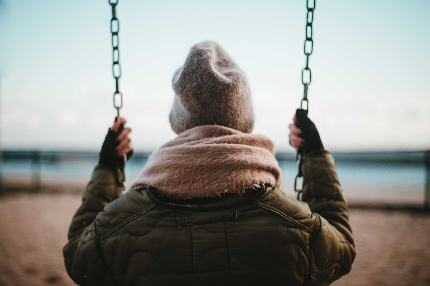 lady wearing hoodie and beanie swinging on swing infront of beach www.oceanrafts.com ocean rafts home page winter collection